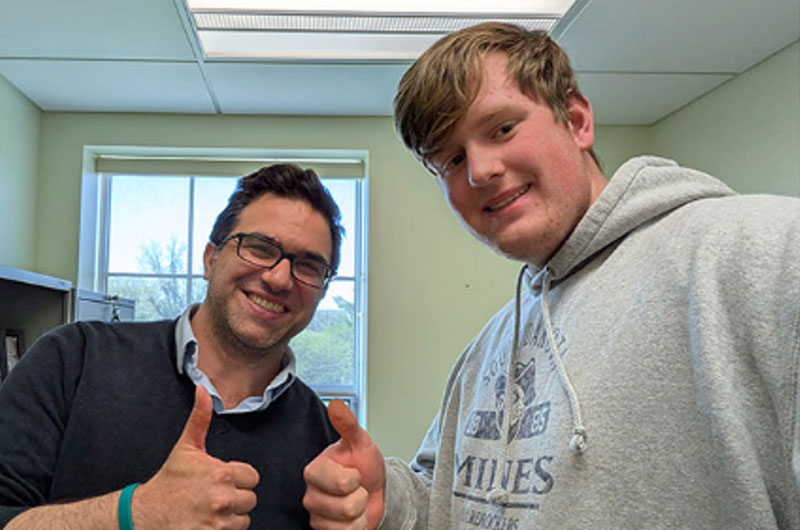 Two men take a selfie and smile while giving a thumbs up