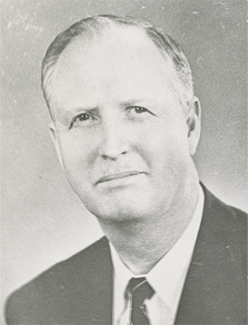 A black and white portrait of Earl Sykes in a black suit and tie from the shoulders up.
