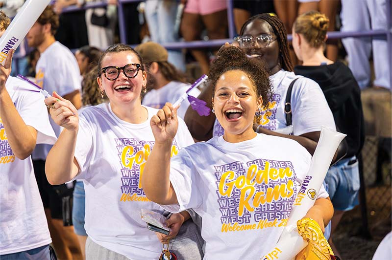 Two students in WCU Welcome Week Golden Rams tshirts are using their WCU purple plastic hand clapper toys and have big smiles on their faces