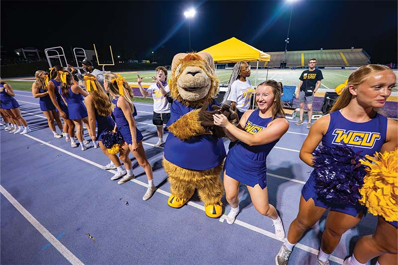 Rammy stands in the line of WCU Cheerleaders and holds hands with one of the cheerleaders
