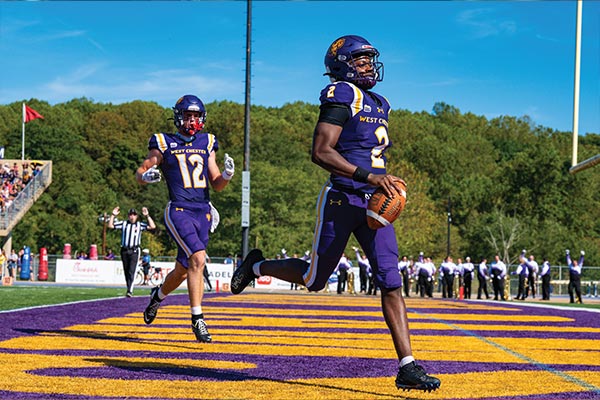 Two football players are in the endzone while the one in front is holding the football