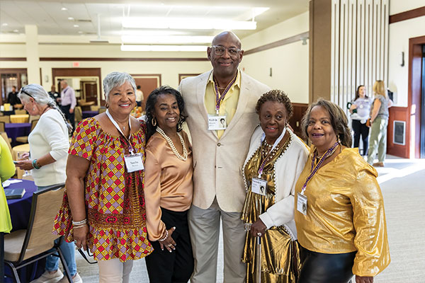A group of well dressed people wearing nametags smile and pose for a photo taken at an indoor seated event