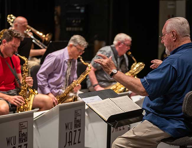 Close up over shoulder of conductor showing saxophone players.