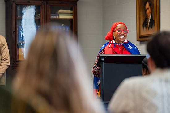 Candid photo from the Frederick Douglass day event. Woman draped in use flag smiling at podium.
